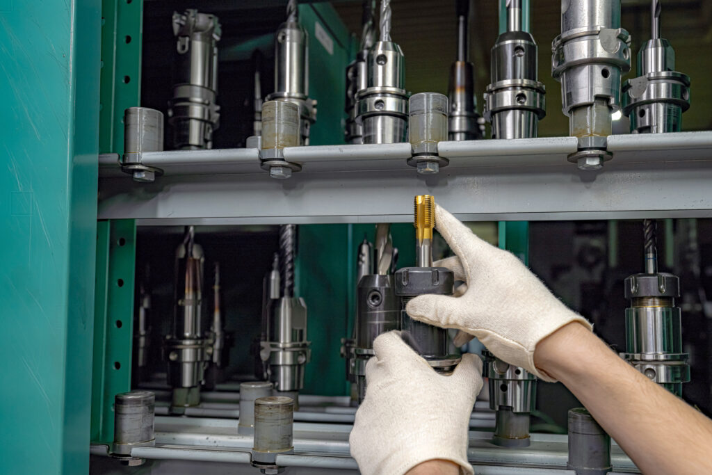 A worker inspects and selects a cutter from a rack to use on a CNC machine.